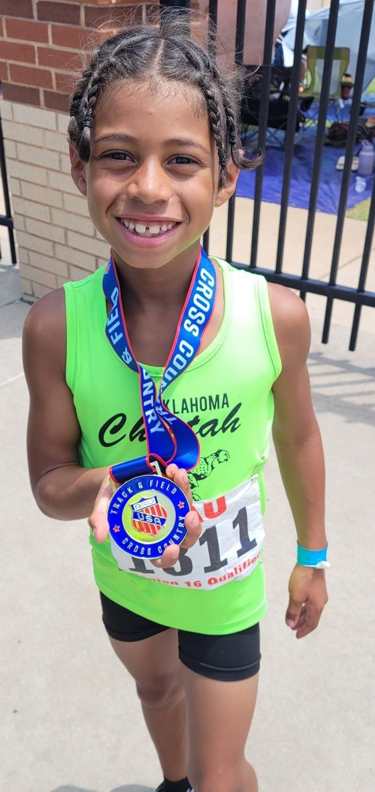 Young Oklahoma Cheetah athlete holding her AAU Cross Country qualifier medal