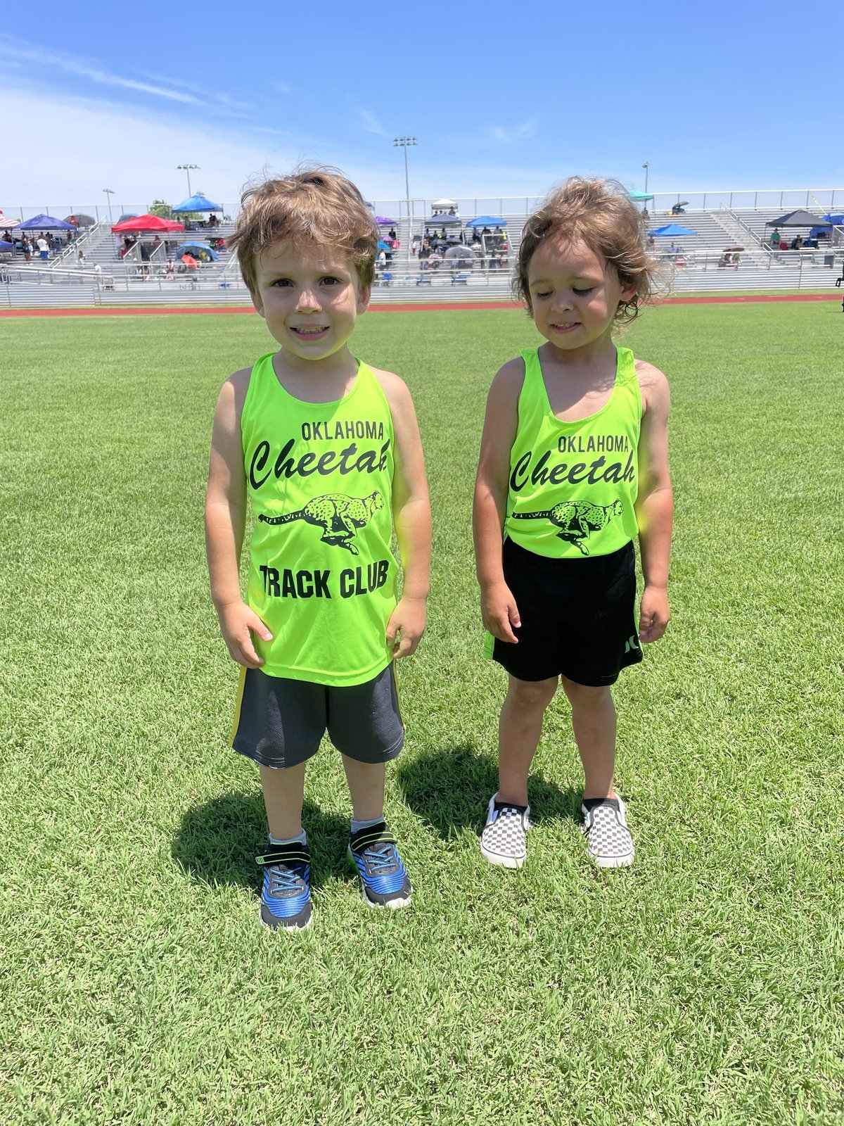 Two young Oklahoma Cheetah Littles in green singlets on the infield at a track meet